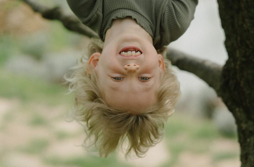 Kind lacht kopfüber vom Baum hängend