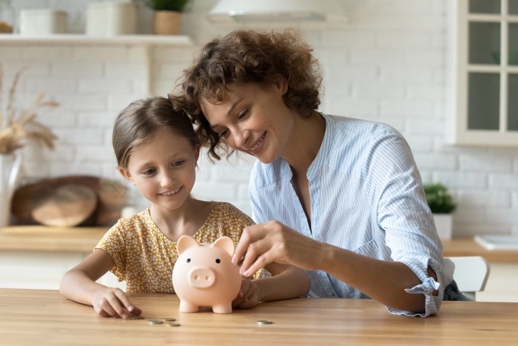 Mama und Tochter werfen Geld in ein Sparschwein
